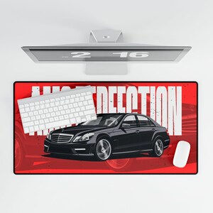 May include: A black car graphic on a red rectangular mousepad with the word "AUTO DECEPTION" in white. A white keyboard and mouse are on the mousepad. A computer monitor is above the mousepad.