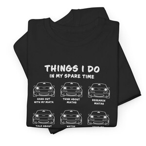 Könnte beinhalten: Schwarzes T-Shirt mit weißem Text und Autoillustrationen. Der Text lautet "THINGS I DO IN MY SPARE TIME" mit Sätzen wie "Hang out with my Miata" und "Think about Miata". Ein humorvolles Design für Autoenthusiasten.