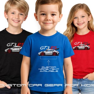 May include: Three children wearing t-shirts with a car graphic. The shirts are black, blue, and red. Each shirt features a white car with red wheels and the text "GT3 RS". The blue shirt has the text "CUSTOM NAME/TEXT AVAILABLE". The bottom of the image reads "CUSTOM CAR GEAR FOR KIDS".