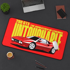 May include: A red mousepad featuring a red sports car illustration with the text "288 GTO UNTOUCHABLE THE GODFATHER OF LEGENDS" in yellow. A white mouse and other office supplies are on the black surface.