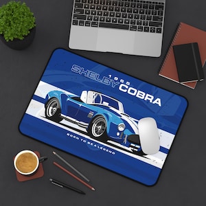 May include: Blue mousepad featuring a vintage Shelby Cobra car illustration. The design includes the text "Shelby Cobra 1965" and "Born to be a Legend" in white. The mousepad has a black border and is on a dark surface.