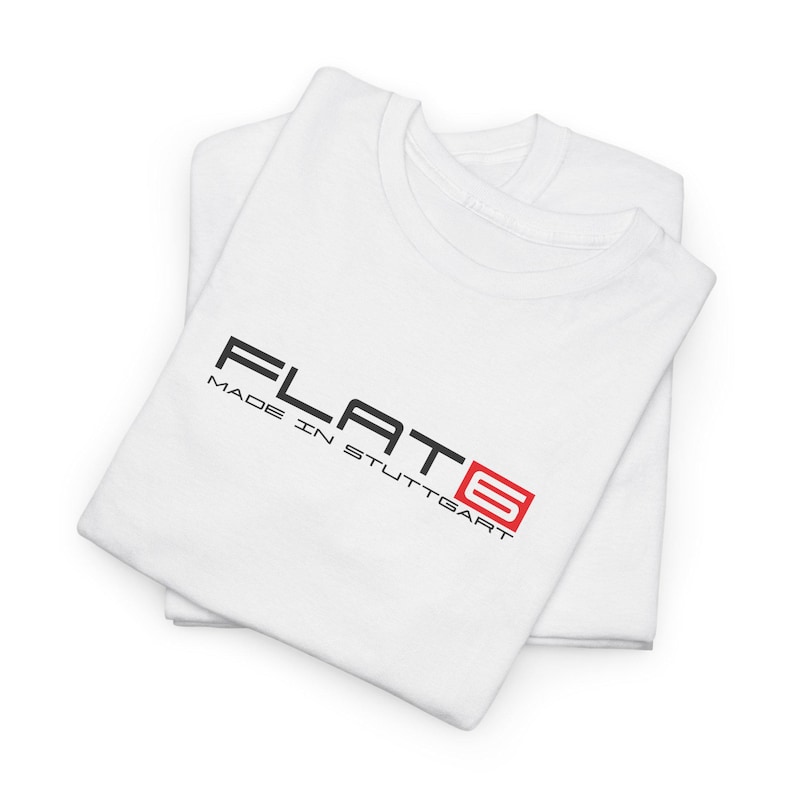 May include: Two white t-shirts are neatly folded and stacked. The top shirt features the text "FLAT6" in black, with the number 6 in a red square, and the words "MADE IN STUTTGART" below it.