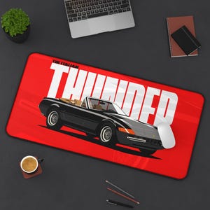 May include: A black convertible car illustration on a red mousepad with the word "THUNDER" in white. The mousepad also has the text "THE ITALIAN". A computer mouse is on the right side of the mousepad.