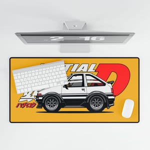 May include: A rectangular yellow desk mat featuring a white car illustration with black wheels and a red "D" graphic. A white keyboard and mouse are on the mat. The text "INITIAL D" is also on the mat.