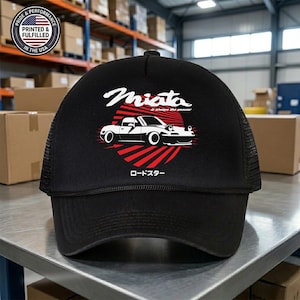 May include: Black trucker hat featuring a white and red graphic of a car with the word "Miata" above it. The text "is always the answer" is also included. The hat has a mesh back and a curved brim.
