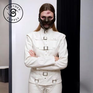 May include: A person wearing a dark brown mask with a mouth opening and a white leather jacket and pants with buckles. The image includes the text "LEATHER SUPPLY" in a circular logo.