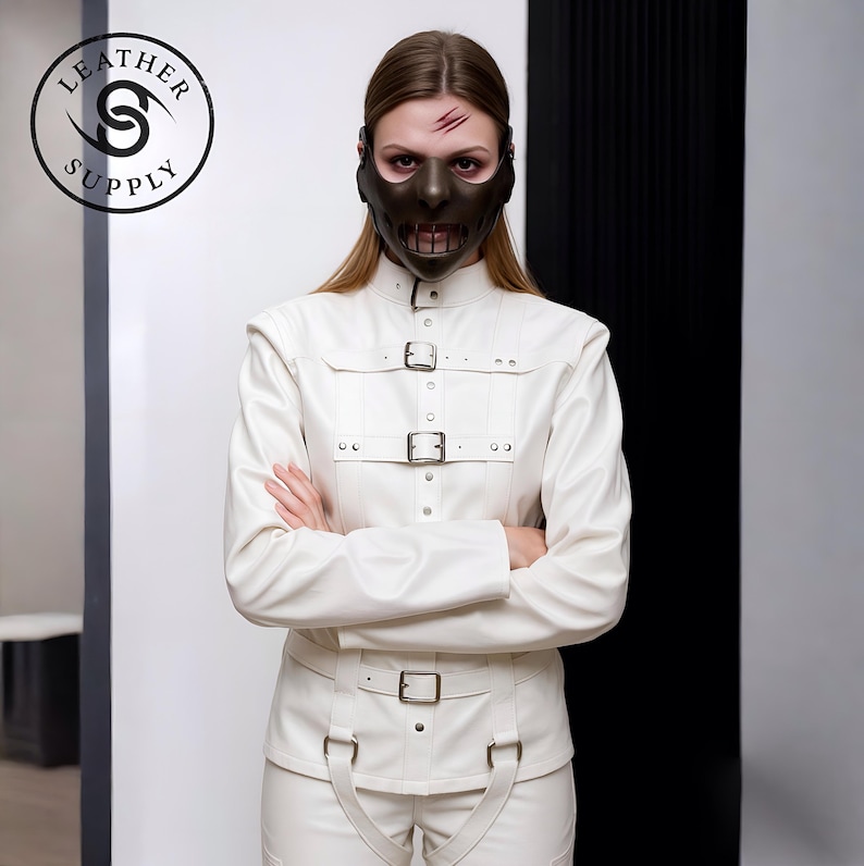 May include: A person wearing a dark brown mask with a mouth opening and a white leather jacket and pants with buckles. The image includes the text "LEATHER SUPPLY" in a circular logo.
