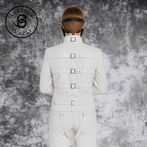 May include: White leather jacket and pants set with multiple straps and buckles. The jacket has three horizontal straps across the back, each secured with a buckle. The pants feature suspender-like straps. The Leather Supply logo is visible.