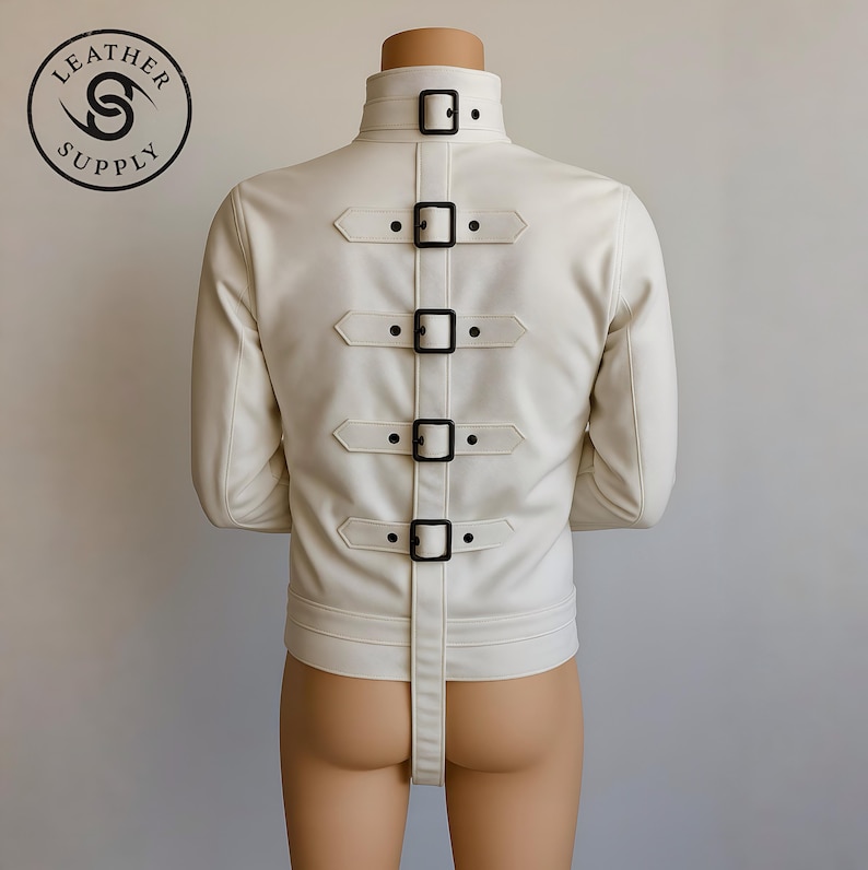 May include: Cream-colored leather jacket with a high collar and multiple black buckle straps down the back. The jacket has long sleeves and a strap that extends from the lower back. The Leather Supply logo is visible in the upper left corner.