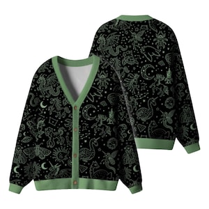 May include: Black cardigan with a green trim and button closure. The sweater features a repeating pattern of mythical creatures, moons, and stars in a light green color. The cardigan is displayed from two angles.
