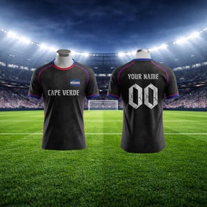 May include: Black football shirt with "CAPE VERDE" and a flag on the front. The back displays "YOUR NAME" above the number "00". The shirt features red and blue trim. The image shows the front and back of the shirt.