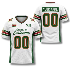 May include: White jersey with green and red accents, featuring the text "Republic of Suriname" and the number "00". The jersey includes the Suriname flag and the text "YOUR NAME" on the back. The design incorporates star and wave patterns.