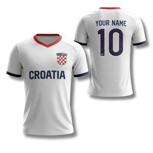 May include: White Croatia football shirt with red and navy blue detailing. The front displays "CROATIA" in navy, a team crest, and a red collar. The back shows "YOUR NAME" above the number "10".