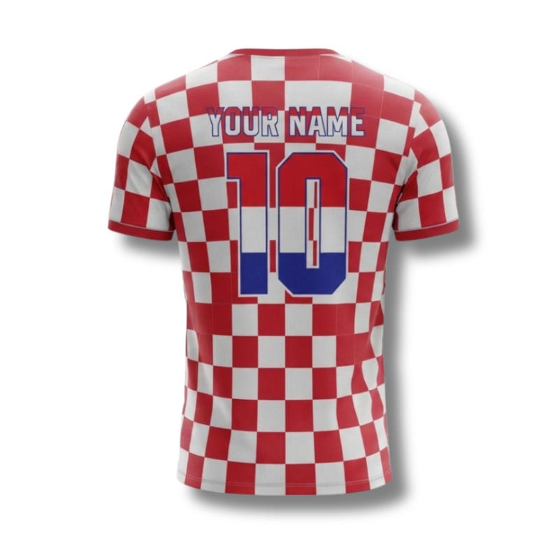 May include: A red and white chequered football shirt featuring the number 10 and the text "YOUR NAME" in white. The number 10 has a blue and red colour scheme. The shirt has short sleeves.