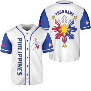 May include: White baseball jersey with blue sleeves and trim. The front features the word "PHILIPPINES" in blue, a map, and the Philippine flag. The back displays a sunburst design and the text "YOUR NAME".