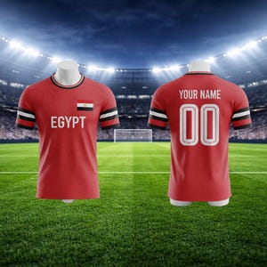 Op de afbeelding: Rood voetbalshirt met het woord "EGYPT" en de Egyptische vlag op de voorkant. De achterkant van het shirt heeft de tekst "YOUR NAME" boven het nummer "00". De mouwen hebben zwart-witte strepen.
