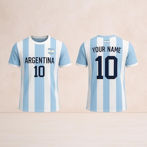以下が含まれることがあります： アルゼンチンの水色と白のストライプのサッカーユニフォーム。前面と背面に番号10。ユニフォームの前面には「ARGENTINA」の文字とアルゼンチンの国旗が表示されています。ユニフォームの背面には「YOUR NAME」の文字があります。