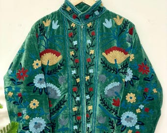 Op de afbeelding: Smaragdgroene fluwelen jas met ingewikkelde bloemenborduurwerk in rood, blauw en goud. De jas heeft een hoge kraag en een ritssluiting over de hele lengte. Het bloemmotief is geconcentreerd op de voorkant en mouwen.