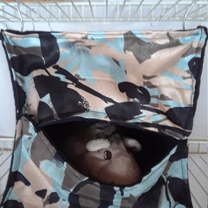 May include: A camouflage-patterned hanging hammock for small pets, with a plush toy inside. The hammock is made of soft fabric and has a black trim.