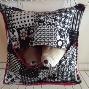May include: A black and white patchwork fabric hanging pouch with a red trim. Two stuffed toys are inside the pouch.