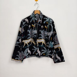 Könnte beinhalten: Schwarze Jacke mit Reißverschluss und Dschungel-Print mit Leoparden, Zebras und Vögeln. Die Jacke hängt an einem Holzkleiderbügel vor einem weißen Hintergrund.