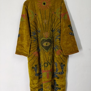 May include: A mustard yellow velvet duster coat featuring intricate embroidery of a central heart with an eye, a sunburst, birds, and cacti. The word LOVE is stitched in dark thread below the heart, with long sleeves and a high collar.