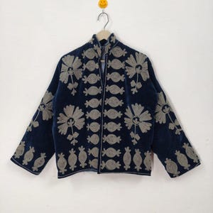 May include: A navy blue jacket with intricate silver floral embroidery. The jacket features a high collar, long sleeves, and a full-length zipper. The floral design is repeated across the front, sleeves, and shoulders, creating a detailed pattern.