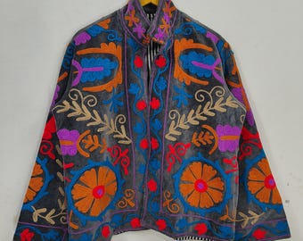 May include: A gray velvet jacket with vibrant floral embroidery in orange, blue, purple, and red. The jacket features a high collar and a button-up front. The embroidery creates a striking contrast against the dark background.