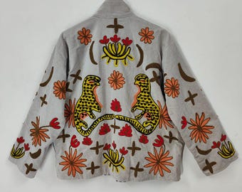 May include: A light grey jacket with colourful embroidery. The back features two yellow and black leopard-like figures facing each other, surrounded by orange and red floral designs and brown crosses.