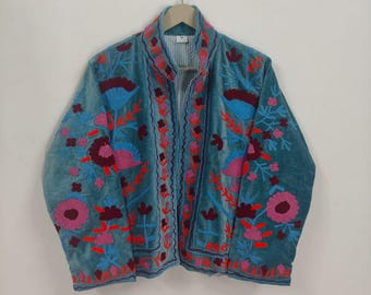 May include: Teal velvet jacket with floral embroidery in shades of pink, red, and blue. The jacket features a mandarin collar and is displayed on a wooden hanger. The embroidery details are visible on the front and sleeves.