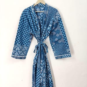 Op de afbeelding: Blauw patroon badjas met een striksluiting, hangend aan een houten hanger. De badjas heeft een mix van patronen, waaronder stippen en wervelende ontwerpen, met witte randen langs de randen. De badjas is gemaakt van een zachte, lichte stof.