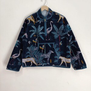 Peut inclure: Veste en velours côtelé bleu marine avec un motif jungle représentant des zèbres, des léopards et des oiseaux parmi des palmiers. La veste a une fermeture éclair, une petite poche et une doublure rayée. Accrochée sur un mur blanc.