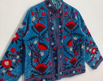 May include: A light blue jacket with intricate floral embroidery in red, burgundy, and white. The jacket features a high collar and long sleeves, with the floral design covering the front, sleeves, and collar. The jacket is hanging on a hanger.