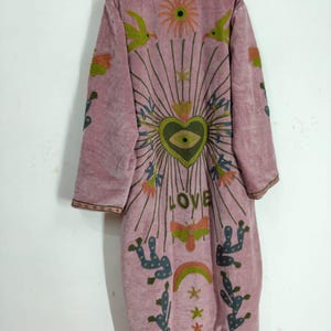 May include: A dusty rose-coloured, long-sleeved coat with intricate embroidery. The design features a central heart with an eye, radiating lines, birds, flowers, and the word "LOVE". The coat has a high collar and a relaxed fit, perfect for layering.