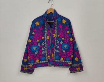 May include: A blue embroidered jacket with a high collar. The jacket features a floral design in pink, yellow, and blue thread. The embroidery is detailed and covers the front and sleeves of the jacket. The jacket is hanging on a wooden hanger.