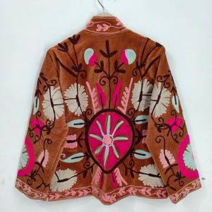 May include: A brown velvet jacket with intricate floral embroidery in pink, light blue, and white. The jacket features a round collar and long sleeves, with detailed patterns on the back and sleeves. The embroidery creates a bohemian aesthetic.