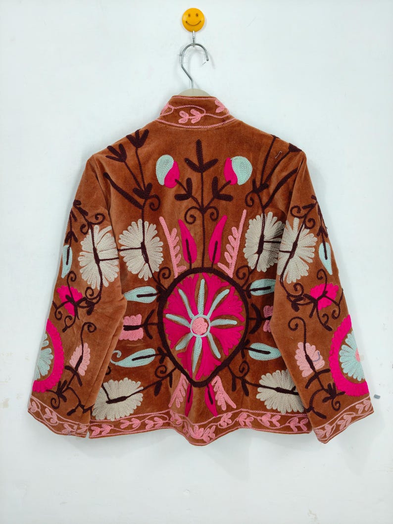 May include: A brown velvet jacket with intricate floral embroidery in pink, light blue, and white. The jacket features a round collar and long sleeves, with detailed patterns on the back and sleeves. The embroidery creates a bohemian aesthetic.