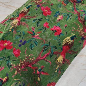 以下が含まれることがあります： 鮮やかな花と鳥の模様の緑色の生地。デザインは、赤いとピンクの花、そして木の枝にとまっているカラフルな鳥が特徴です。生地は柔らかく、ビロードのような質感です。