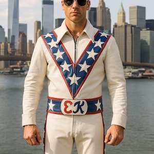 May include: Cream-colored jumpsuit with a star-spangled design. The jacket has a blue and red chevron pattern with white stars. A matching belt with the initials "EK" completes the look. The outfit is worn with sunglasses.