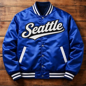 Könnte beinhalten: Königsblaue Satinjacke mit dem Wort "Seattle" in weißer Schrift auf der Brust. Die Jacke hat weiß-marineblaue Streifen an Kragen, Manschetten und Bund sowie weiße Paspeltaschen.