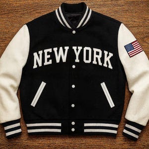 Può includere: Giacca college nera con maniche bianche. La giacca presenta la scritta "NEW YORK" in bianco, una toppa con la bandiera americana e strisce bianche sui polsini e sull'orlo.