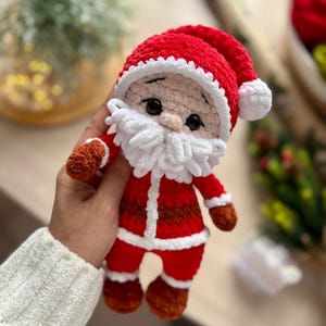 Puede incluir: Mu&ntilde;eco de Pap&aacute; Noel tejido a ganchillo, rojo y blanco. Tiene barba blanca, manos y pies marrones, y ojos negros. Un gorro rojo completa el dise&ntilde;o. Una decoraci&oacute;n navide&ntilde;a festiva.