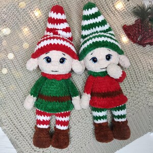 May include: Two handmade crochet elf dolls. One elf wears a red and white striped hat, green top, red and white striped pants, and brown boots. The other elf wears a green and white striped hat, red top, green and white striped pants, and brown boots.