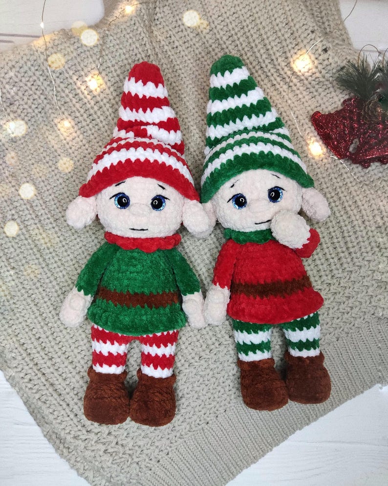 May include: Two handmade crochet elf dolls. One elf wears a red and white striped hat, green top, red and white striped pants, and brown boots. The other elf wears a green and white striped hat, red top, green and white striped pants, and brown boots.