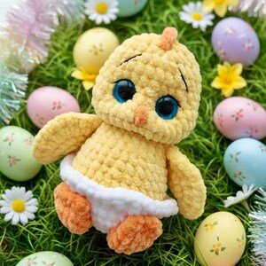 Pode incluir: Um pintinho amarelo feito &agrave; m&atilde;o em croch&ecirc; com grandes olhos azuis, bico e p&eacute;s laranja e uma fralda branca. O pintinho &eacute; cercado por ovos de P&aacute;scoa decorados em cores pastel, margaridas e flores amarelas, tudo sobre grama verde.
