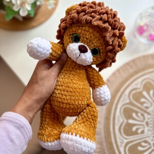 May include: A handmade plush lion with a golden-yellow body, brown mane, and white paws. The lion has large green eyes and a brown nose. This soft toy is a cute and cuddly item.