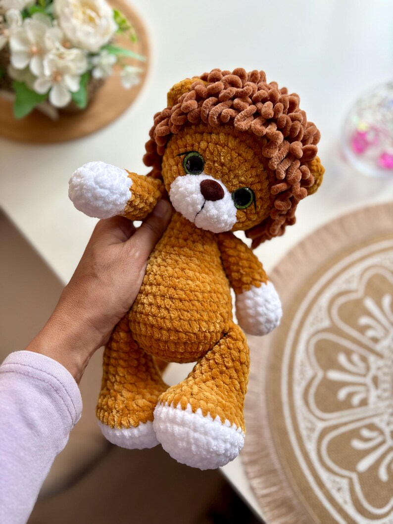 May include: A handmade plush lion with a golden-yellow body, brown mane, and white paws. The lion has large green eyes and a brown nose. This soft toy is a cute and cuddly item.