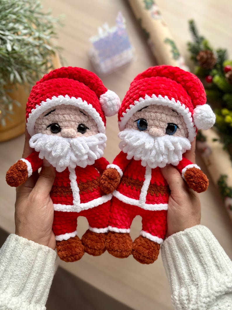 Puede incluir: Dos mu&ntilde;ecos de Pap&aacute; Noel hechos a mano con ganchillo. Cada mu&ntilde;eco tiene un traje rojo con ribetes blancos, una barba blanca y un gorro rojo con un pomp&oacute;n blanco. Los mu&ntilde;ecos se sostienen delante de un fondo borroso.