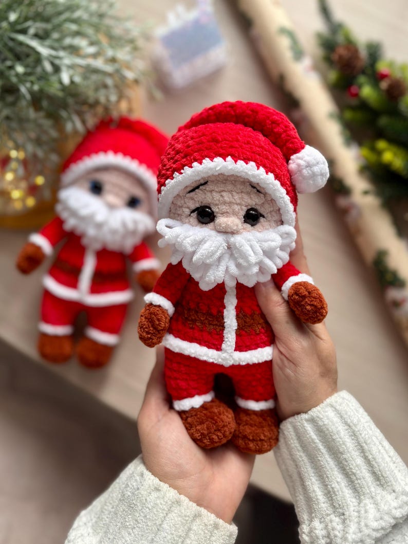 Puede incluir: Dos mu&ntilde;ecos de Pap&aacute; Noel hechos a mano con ganchillo. Cada mu&ntilde;eco tiene un traje rojo, gorro y botas y guantes marrones. Los mu&ntilde;ecos tienen barbas blancas y caras sonrientes. Uno est&aacute; enfocado, el otro ligeramente borroso.