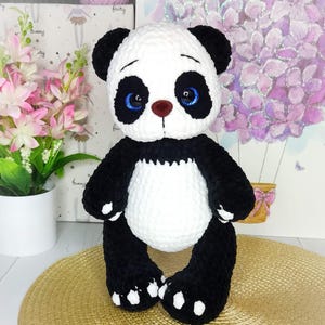 May include: A handcrafted panda bear soft toy in black and white. The panda has black ears, limbs, and a white body and head. It has blue eyes and a brown nose. The plush toy is designed to stand upright, a charming decorative item.